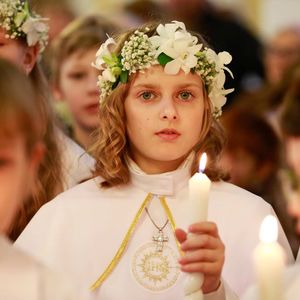 Mädchen mit Blumenschmuck bei Erstkommunion hält Kerze